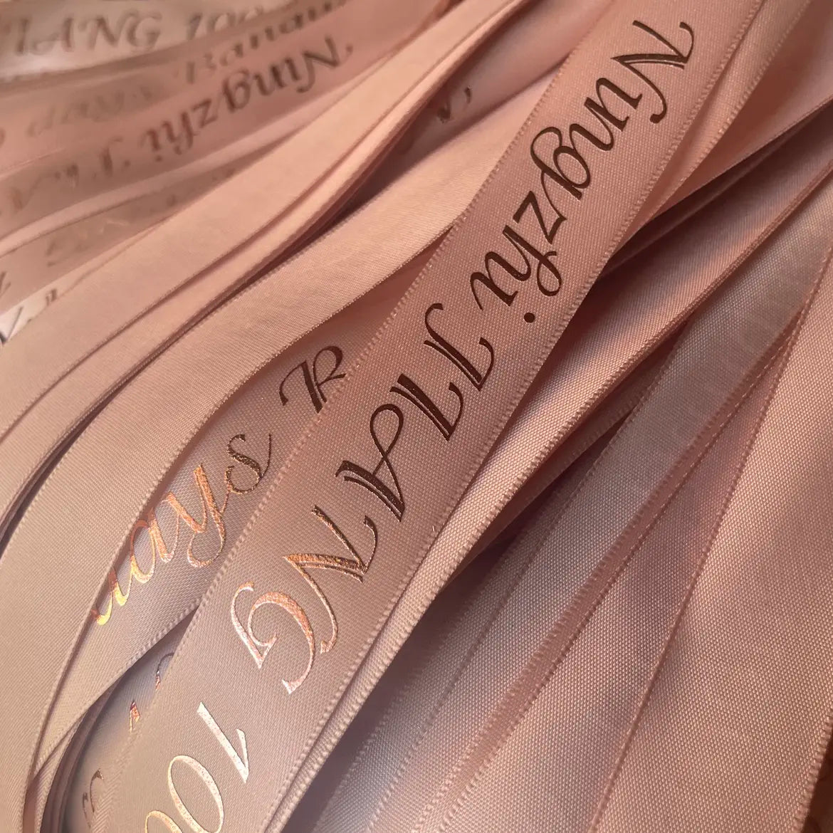 Custom polyester cotton ribbon in soft blush pink with elegant gold lettering for gift wrapping and branding.