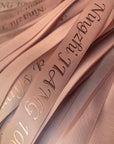 Custom polyester cotton ribbon in soft blush pink with elegant gold lettering for gift wrapping and branding.