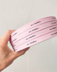 Hand holding custom pink cotton ribbon featuring personalized text for packaging and crafts.