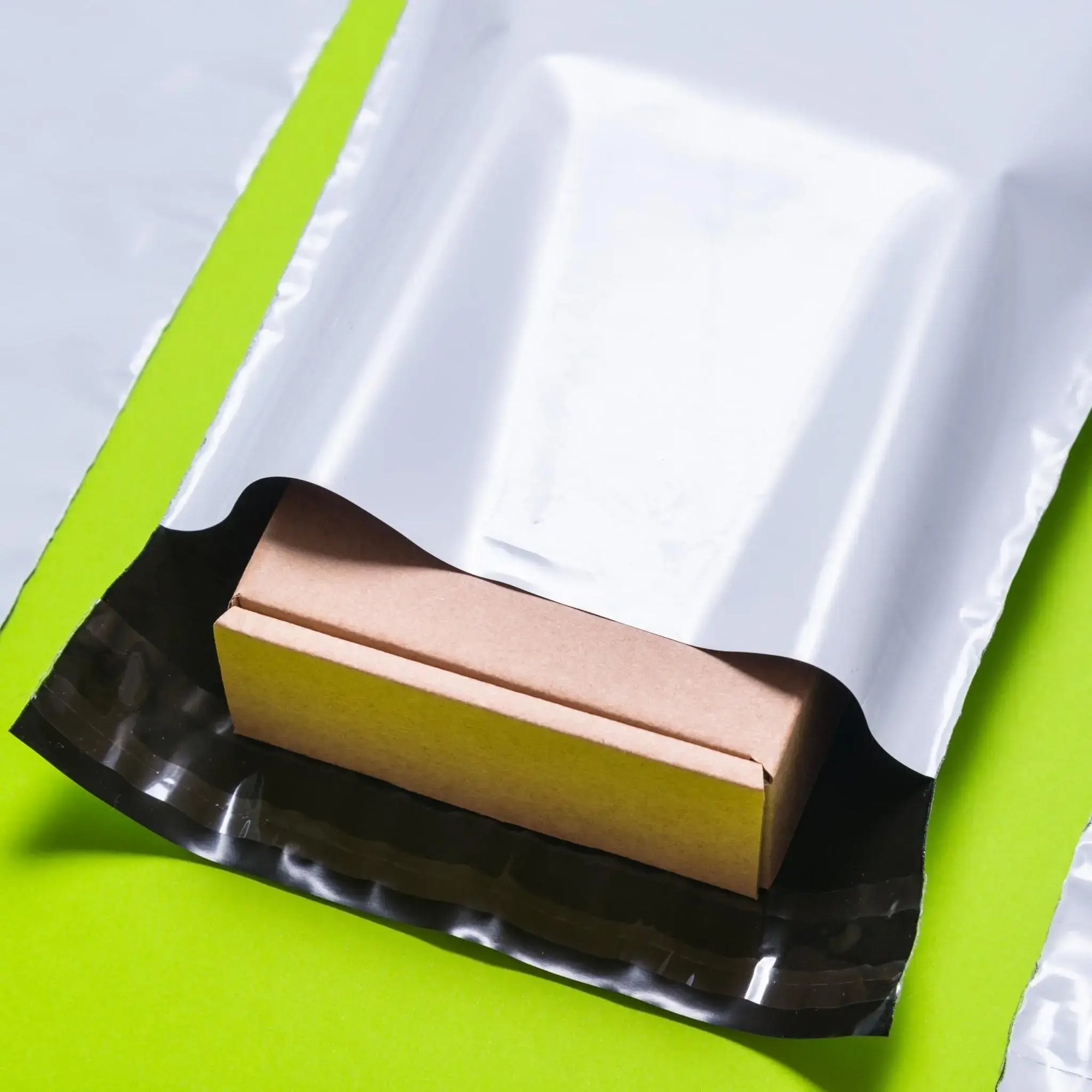 Durable wholesale poly mailer with a self-sealing adhesive strip, featuring a small cardboard box inside.