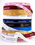 Stack of colorful custom grosgrain ribbons featuring various logos and text, ideal for crafting and branding.