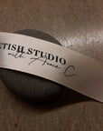 Custom satin ribbon featuring "Fetish Studio with Annie C" logo on a smooth stone background.