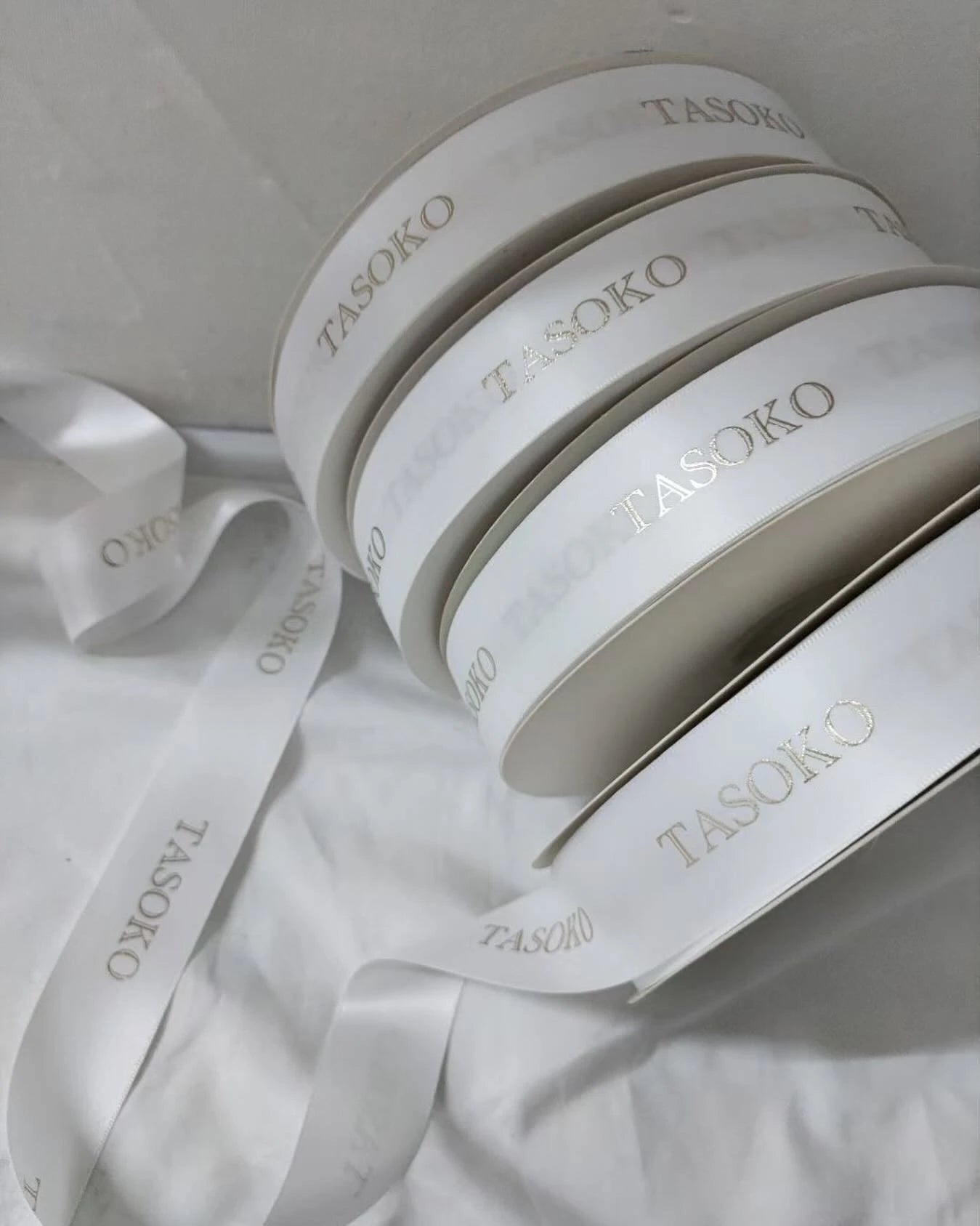 Custom satin ribbon rolls with embossed "TASOKO" logo, featuring a soft, luxurious finish. Perfect for gifts and decorations.